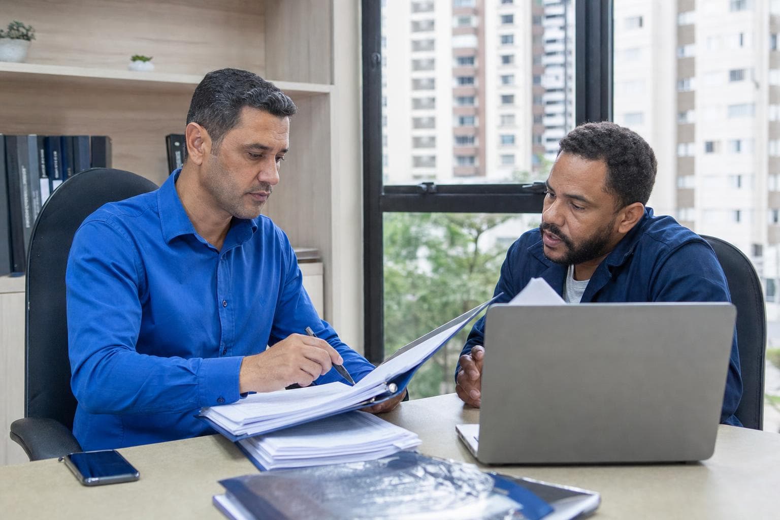 Gerente de administradora revisando pastas e laptop com uma síndica no escritório
