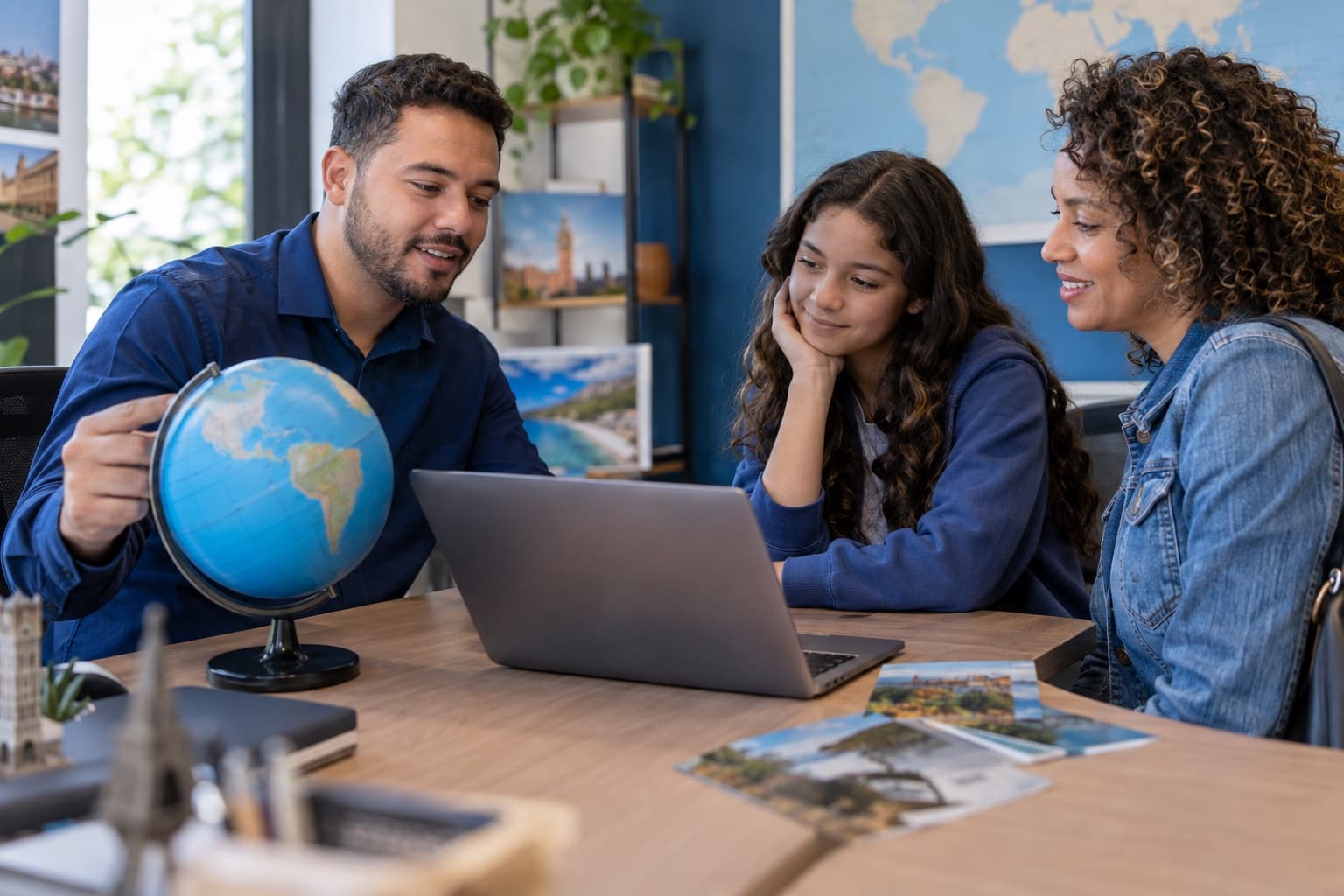 Consultora mostrando um globo e um notebook a uma adolescente e à mãe em escritório de agência de intercâmbio