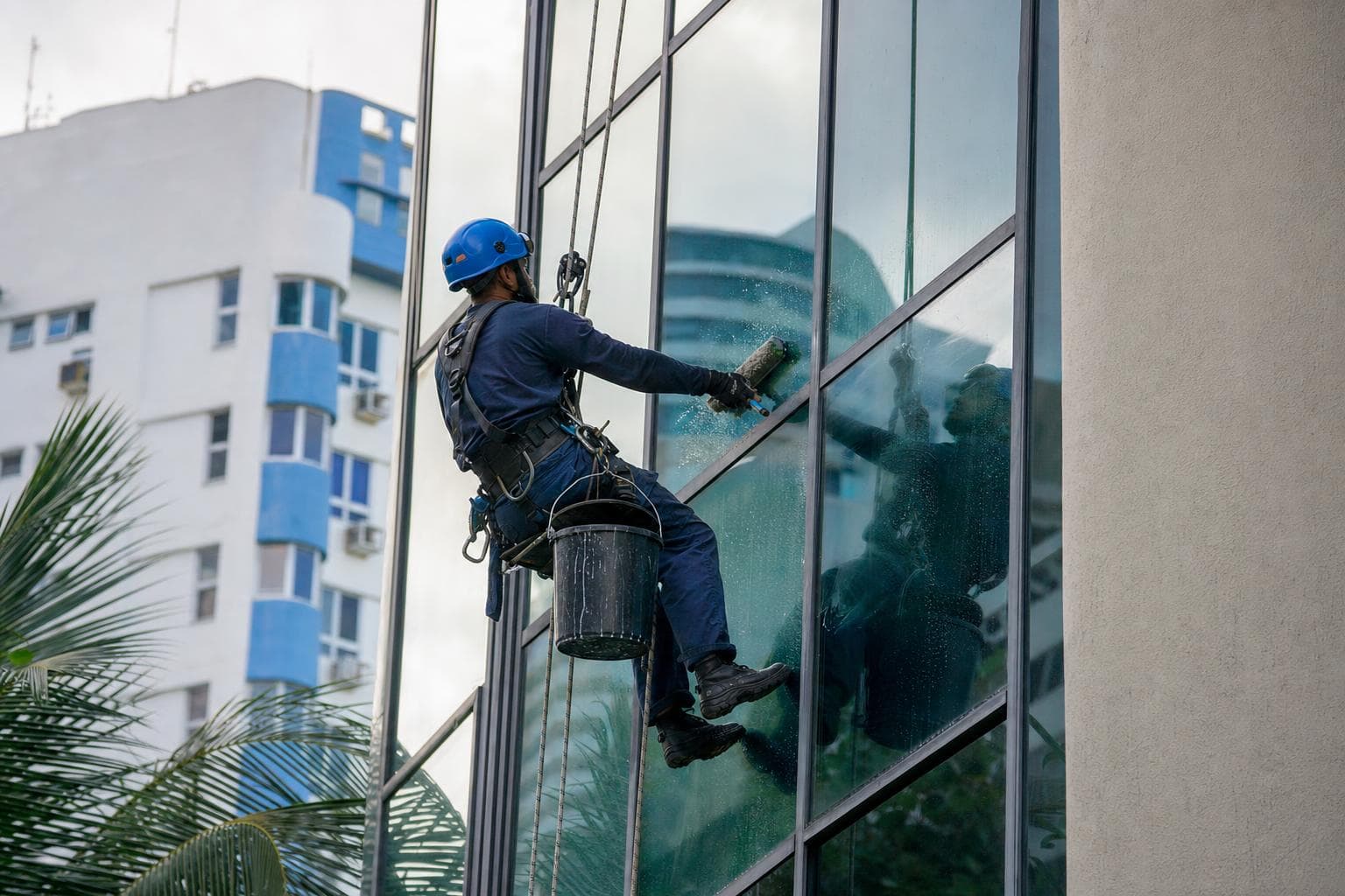 Alpinista industrial suspenso por cordas limpando os vidros da fachada de um prédio comercial