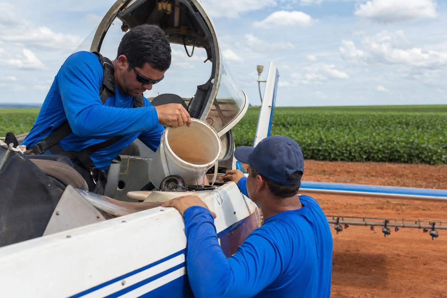 Piloto e técnico abastecendo um avião agrícola de pulverização em uma pista de terra