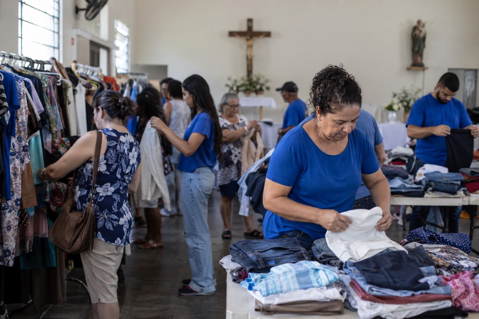 Voluntárias arrumando roupas doadas em araras e mesas de um bazar beneficente no salão paroquial