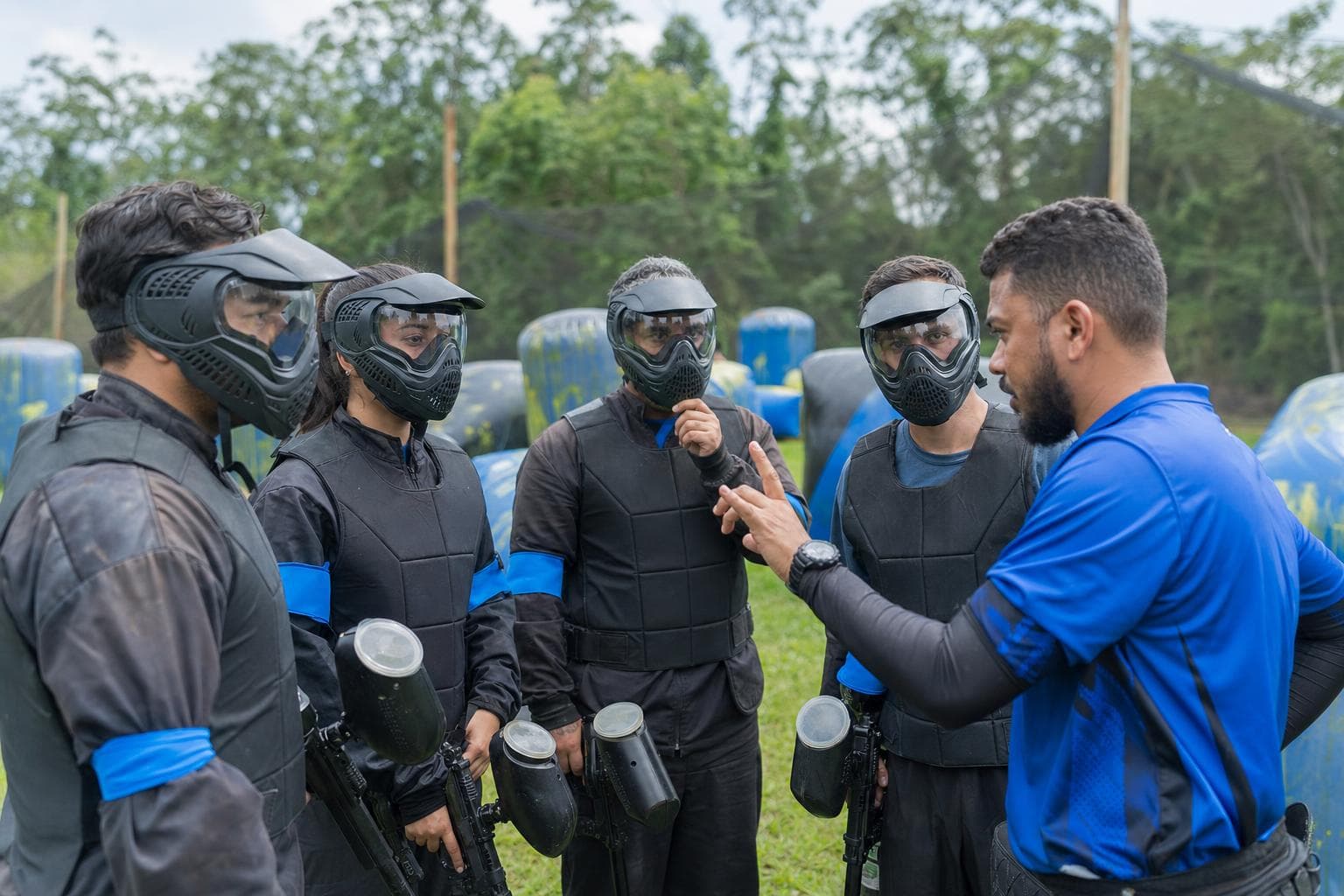 Jogadores de paintball com máscaras recebendo instruções do juiz antes da partida