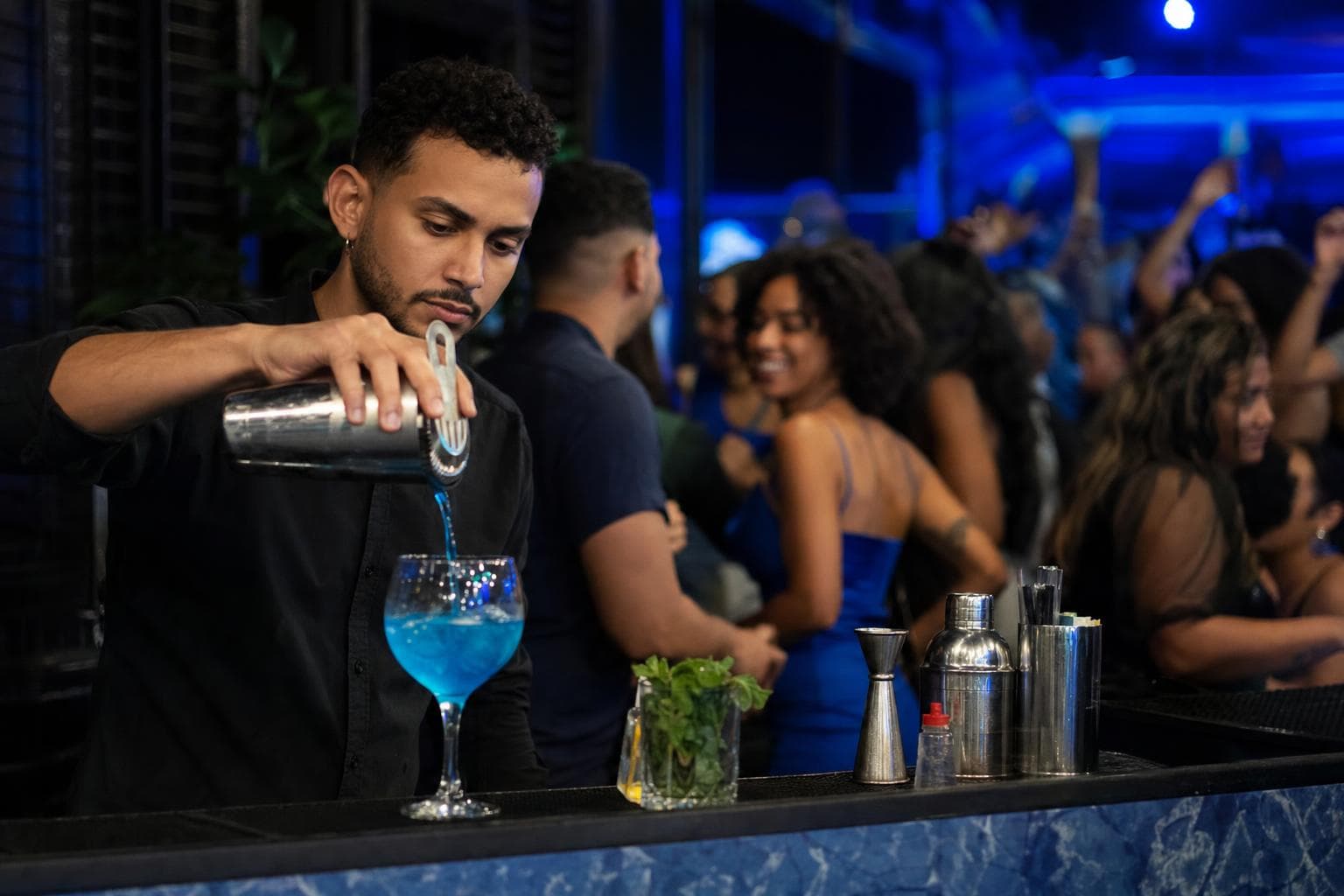 Bartender servindo drinks no balcão de uma casa noturna com iluminação azul
