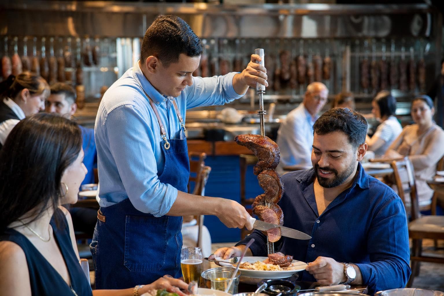 Passador de carne servindo picanha no espeto à mesa de uma churrascaria