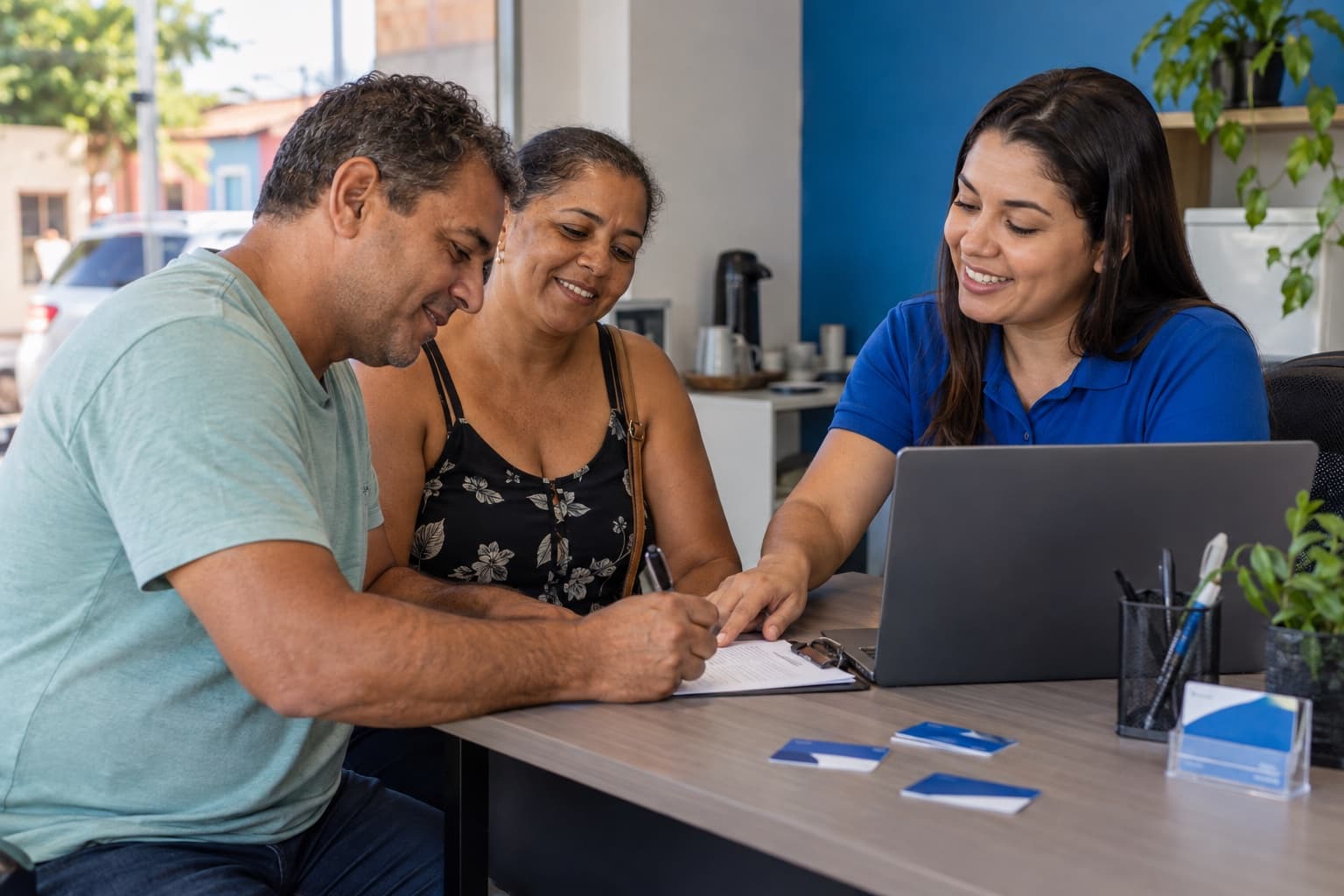 Atendente de camisa azul cadastrando casal em cartão de desconto em escritório pequeno