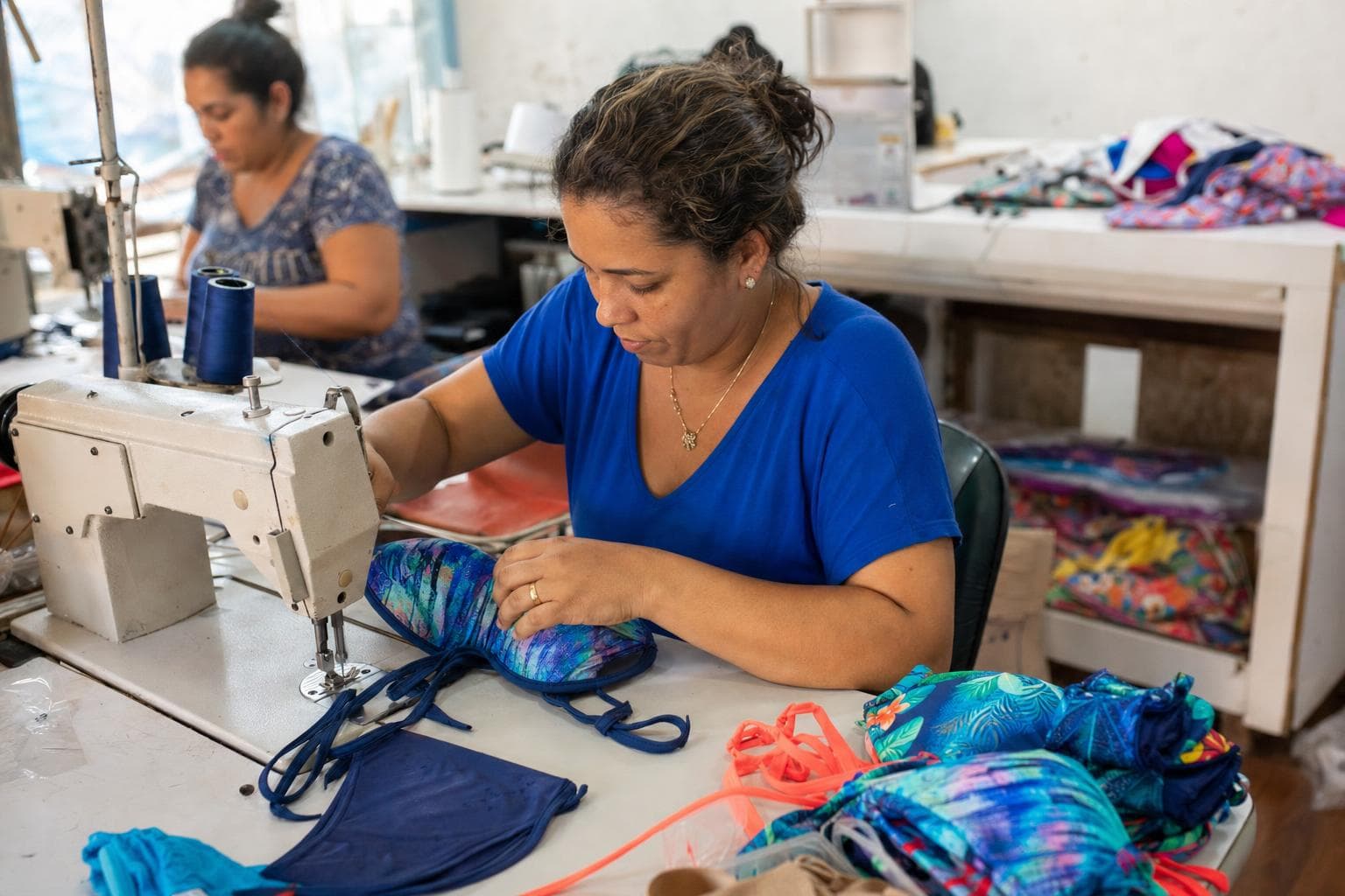 Costureira ajustando o bojo de um biquíni na máquina de costura com peças de moda praia sobre a mesa