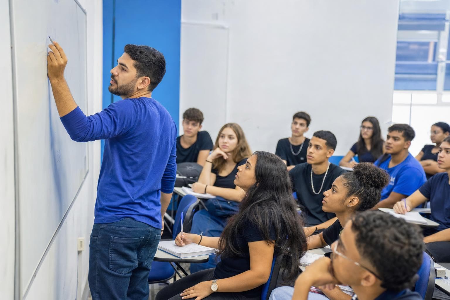 Professor explicando uma questão de física no quadro para uma turma de cursinho
