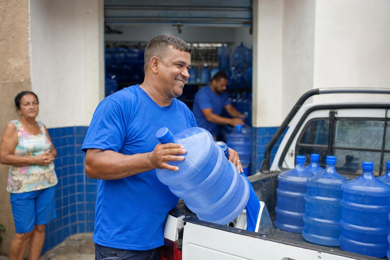 Entregador carregando galões de água mineral de 20 litros na caçamba de uma picape