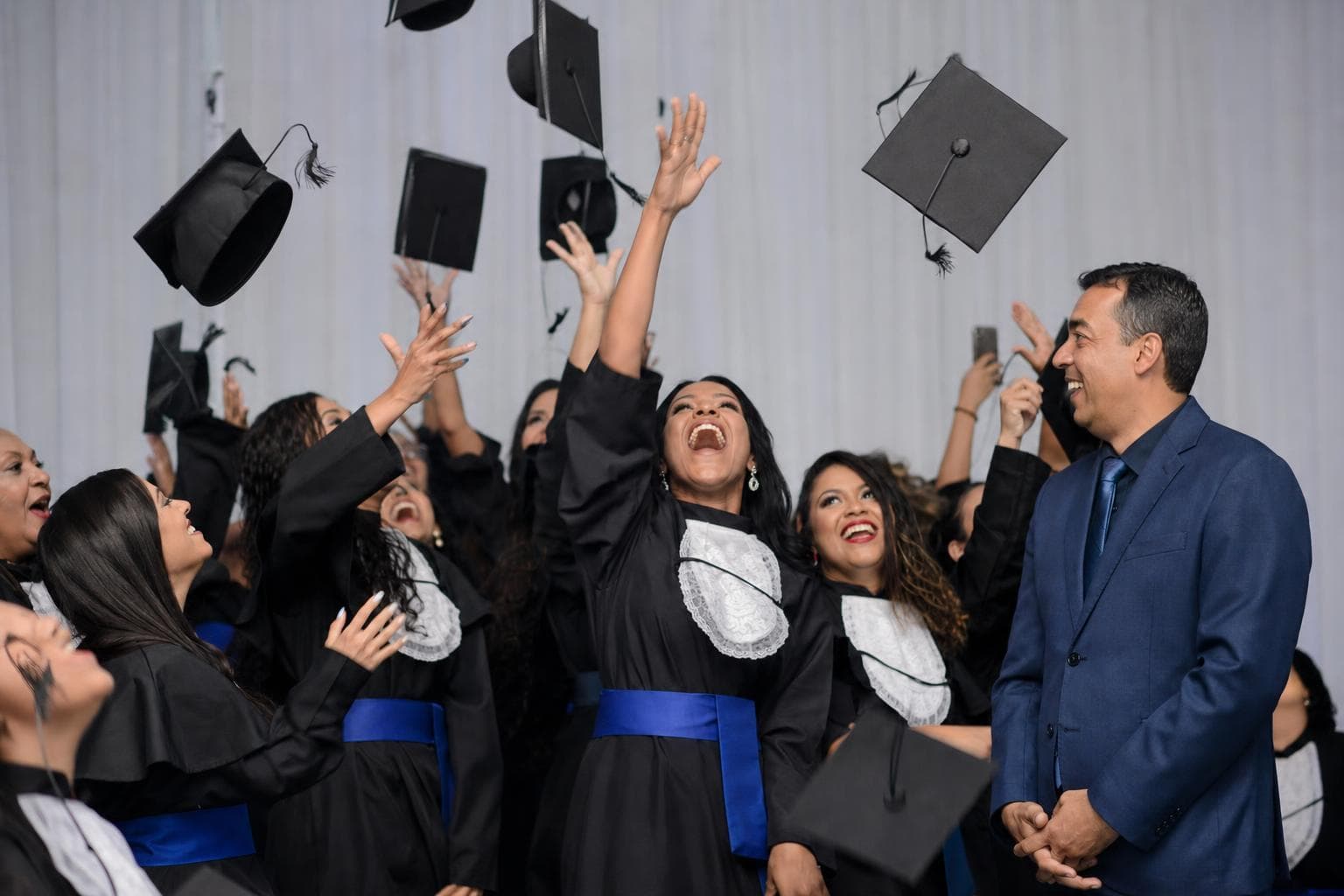 Formandos de beca jogando capelos para cima em um salão de festa de formatura