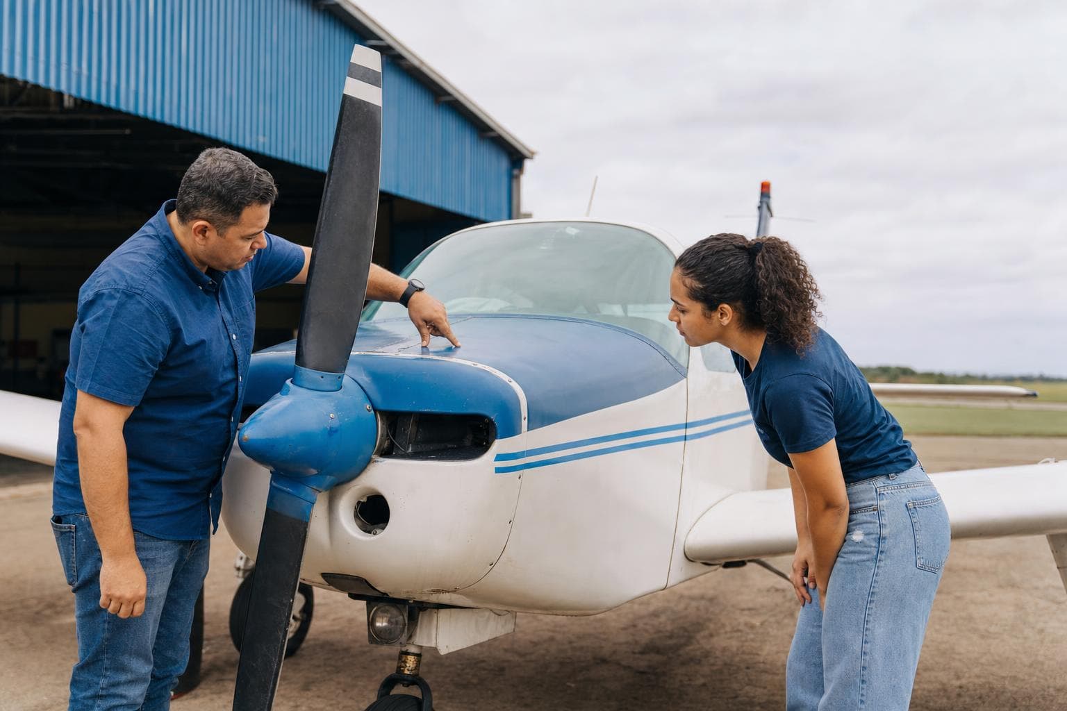 Instrutor de voo e aluno fazendo a inspeção externa de um avião monomotor ao lado do hangar
