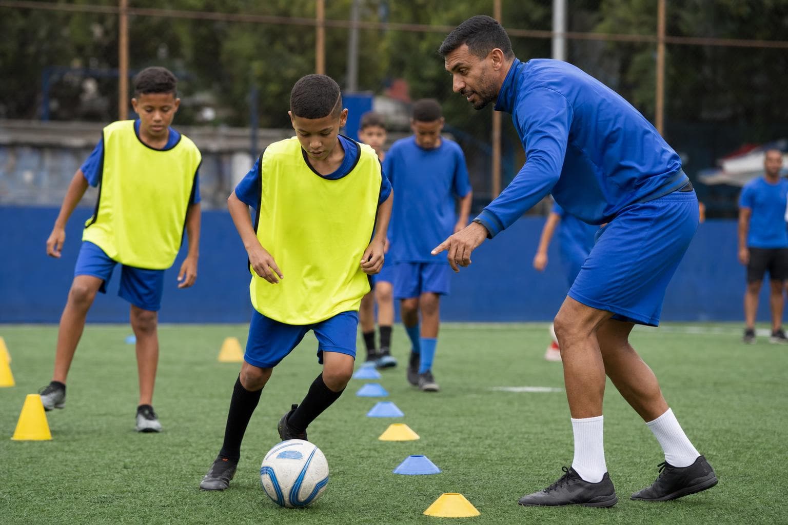 Treinador orientando crianças em um treino de escolinha de futebol no campo sintético