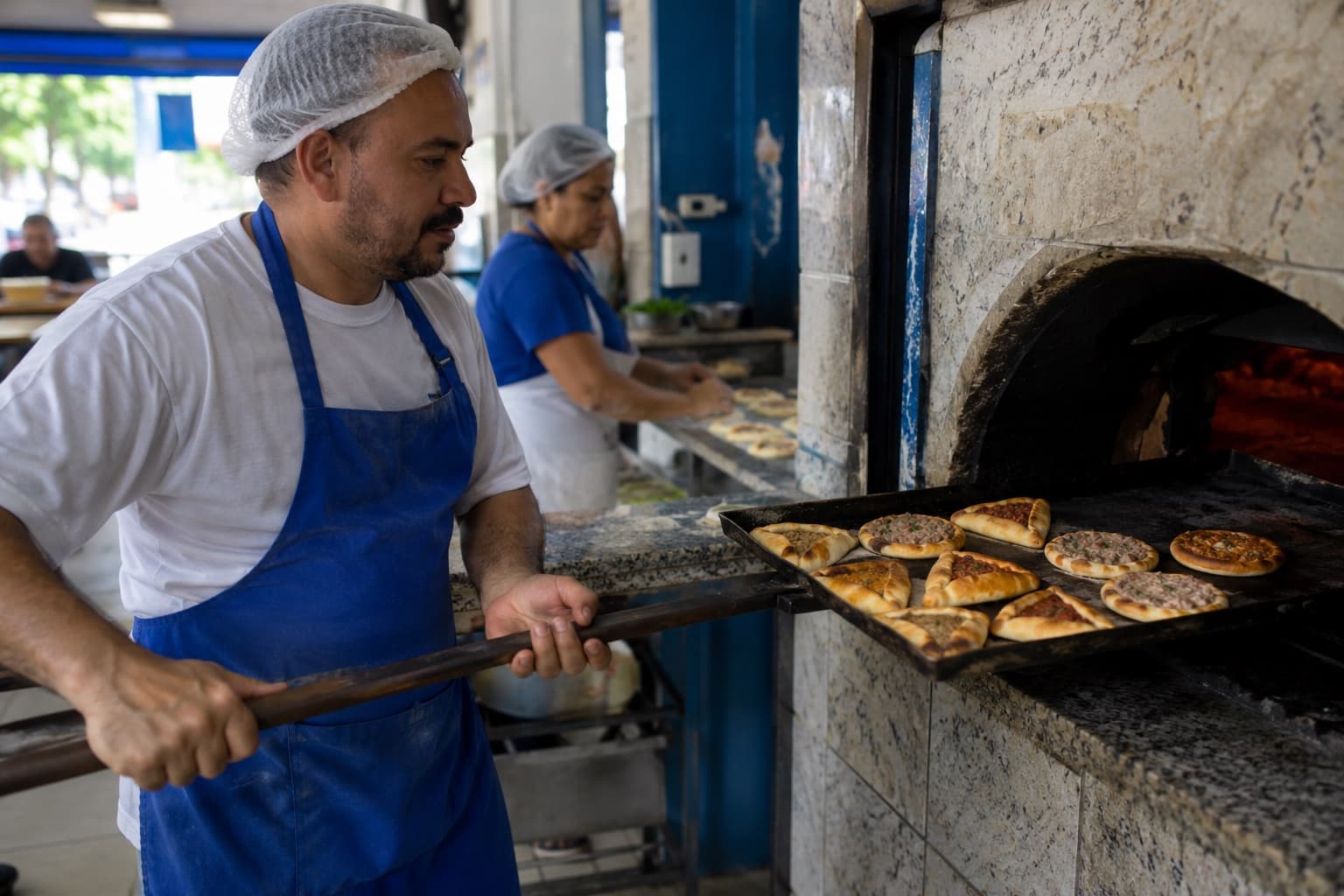 Cozinheiro retirando do forno uma assadeira com esfihas abertas e fechadas