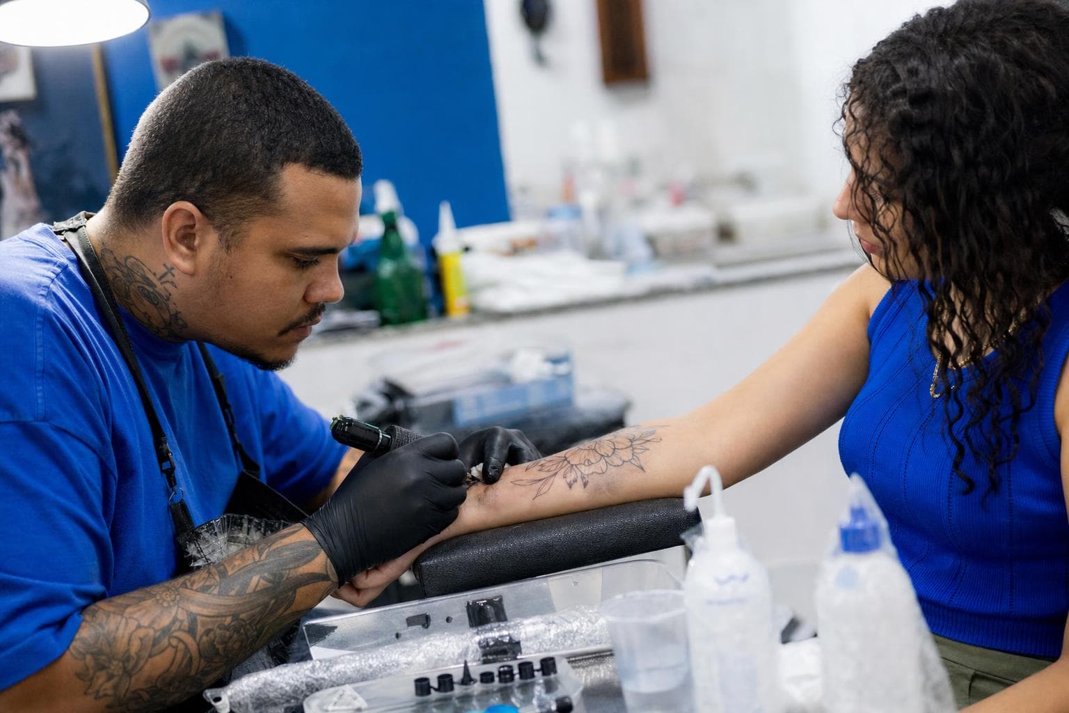 Tatuador trabalhando no braço de um cliente em um estúdio de tatuagem