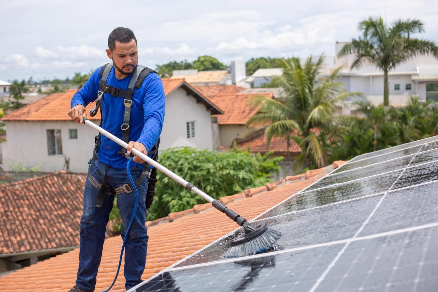 Técnico limpando placas solares com escova de cerdas macias e água em um telhado residencial