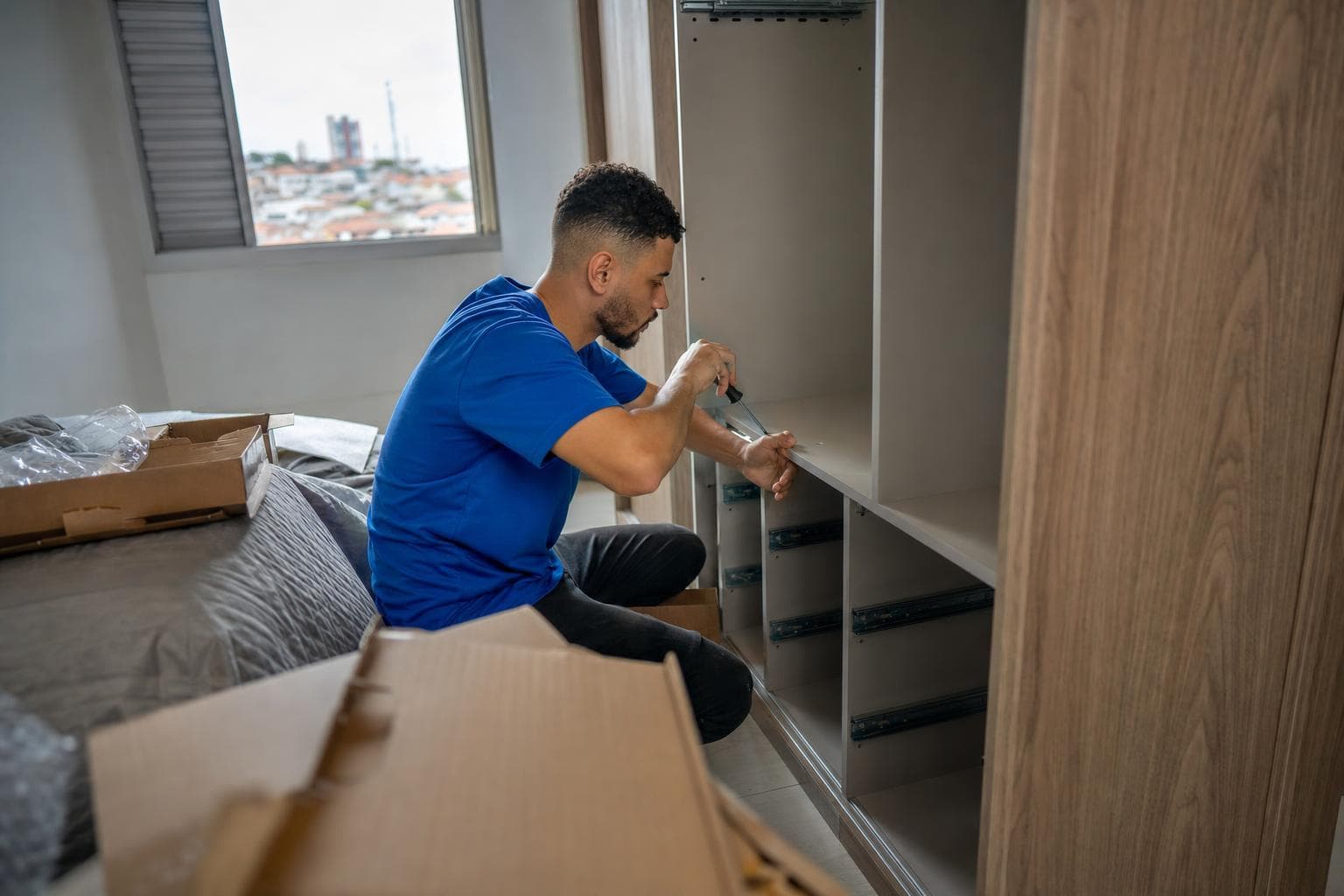 Montador de móveis montando um guarda-roupa em um quarto com caixas de papelão abertas