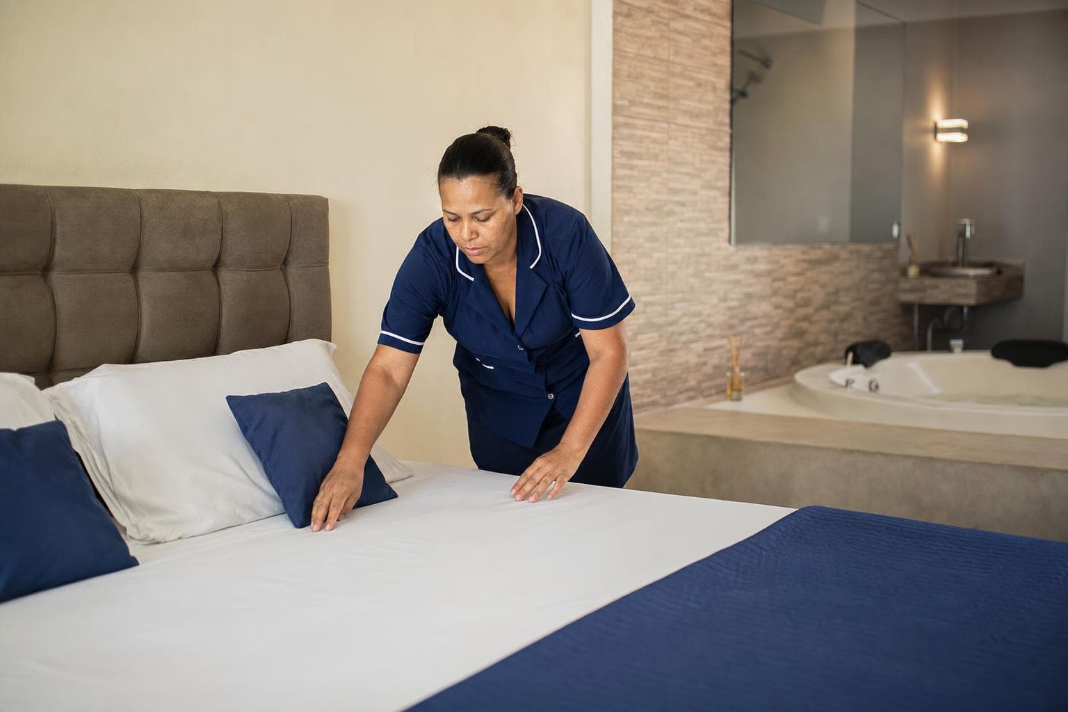 Camareira arrumando a cama de uma suíte com iluminação suave em um motel
