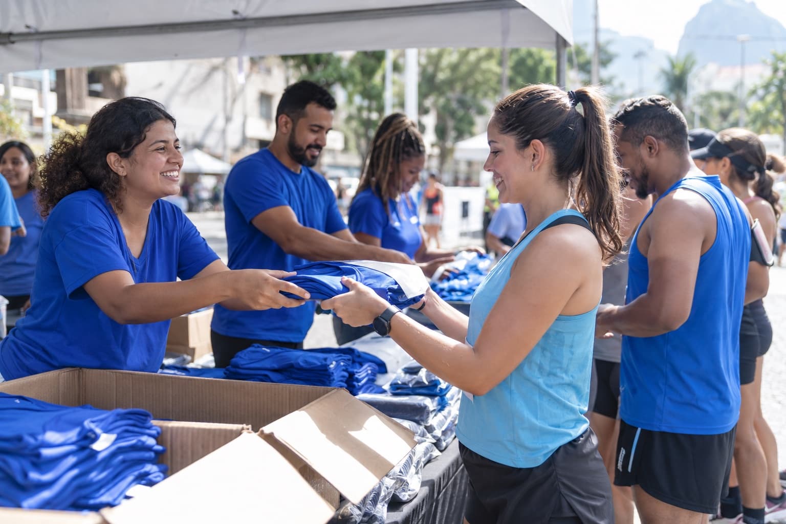 Voluntários entregando kits com camisetas a corredores numa tenda de retirada antes de uma corrida de rua