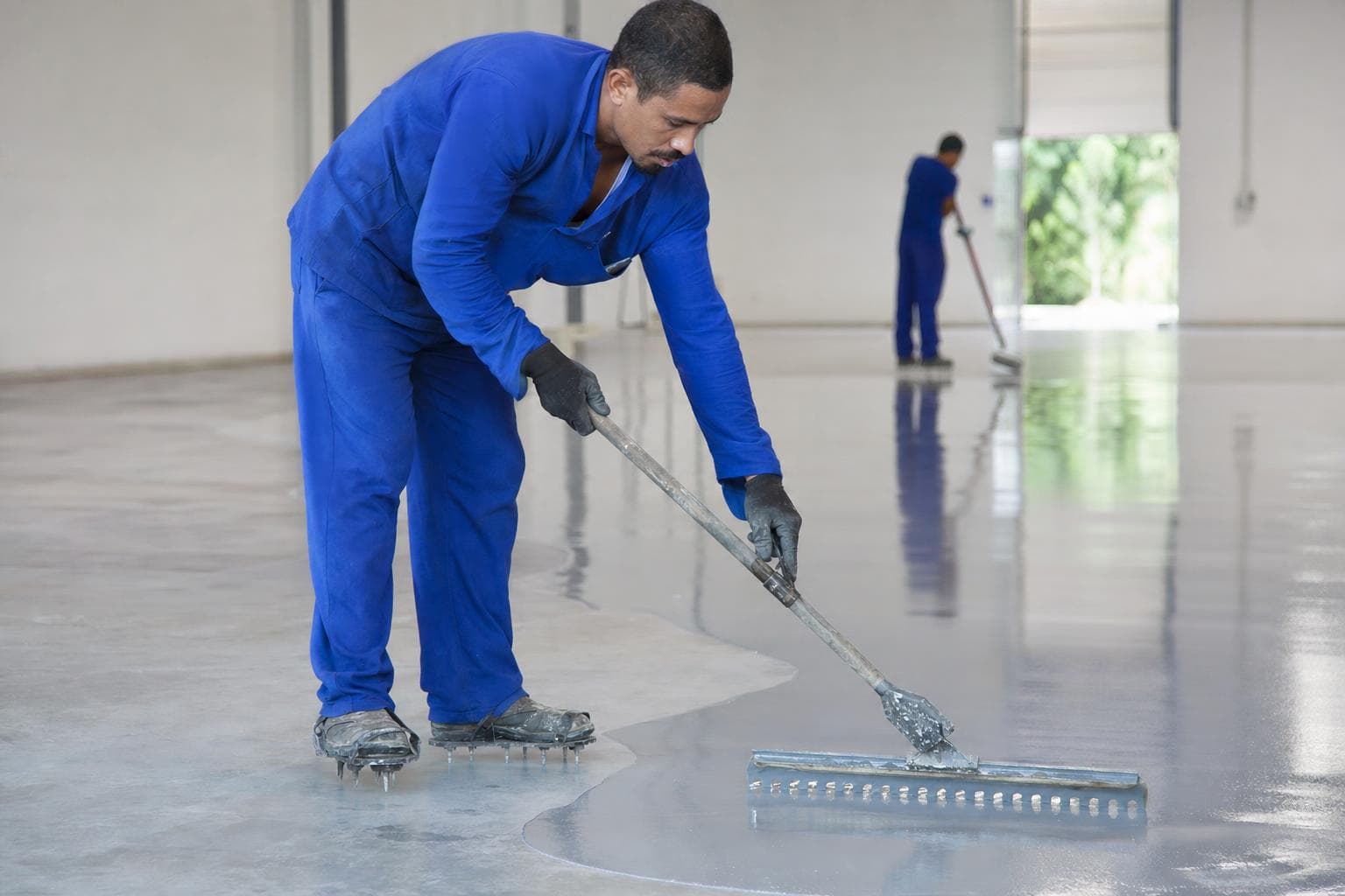 Aplicador espalhando resina epóxi com rodo dentado sobre piso de concreto em galpão