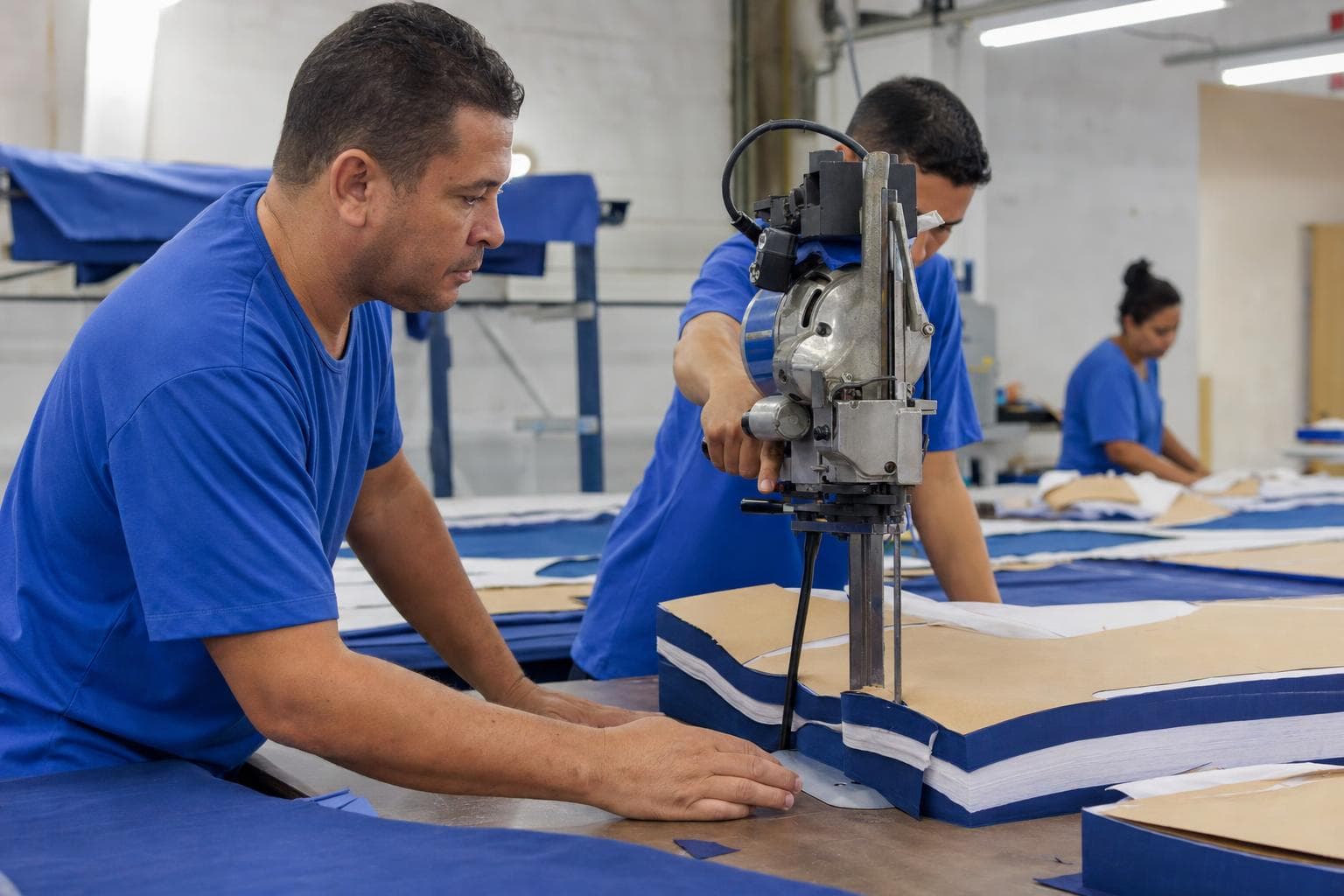 Cortador acompanhando a máquina de corte automático cortando o enfesto de tecido sobre a mesa longa