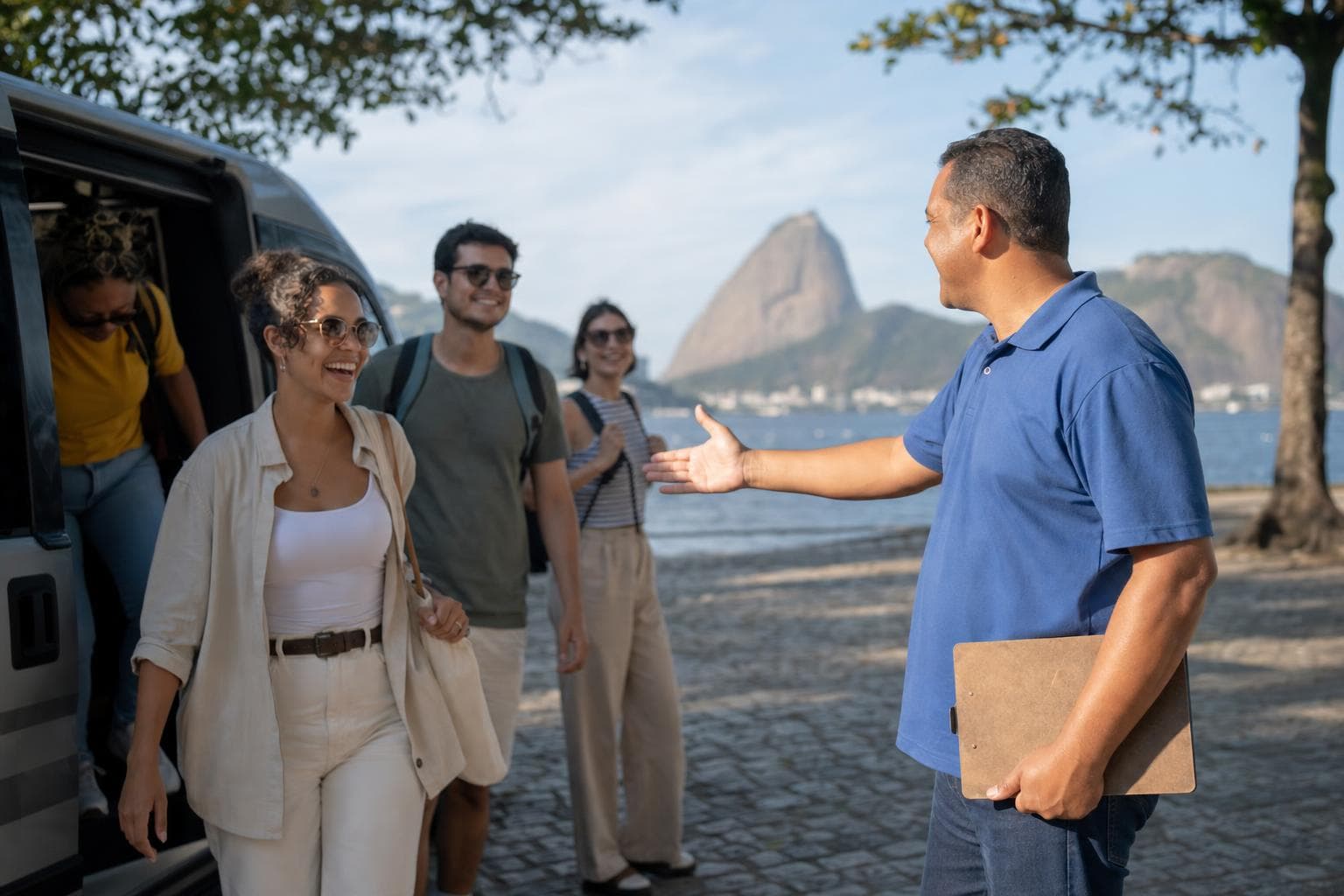Guia de turismo recebendo um grupo de turistas ao lado de uma van em uma orla