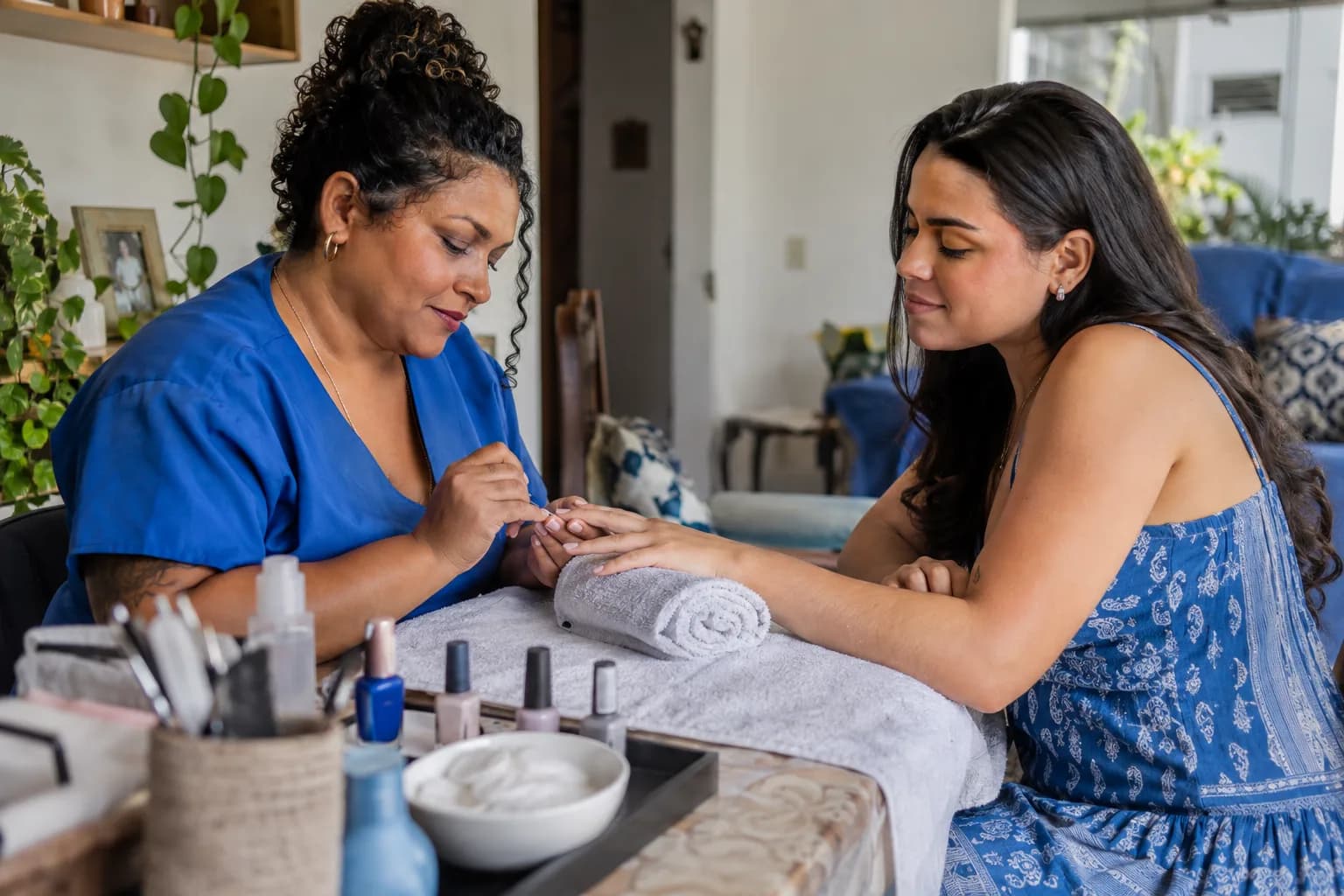 Manicure atende uma cliente numa mesa em casa com luz natural