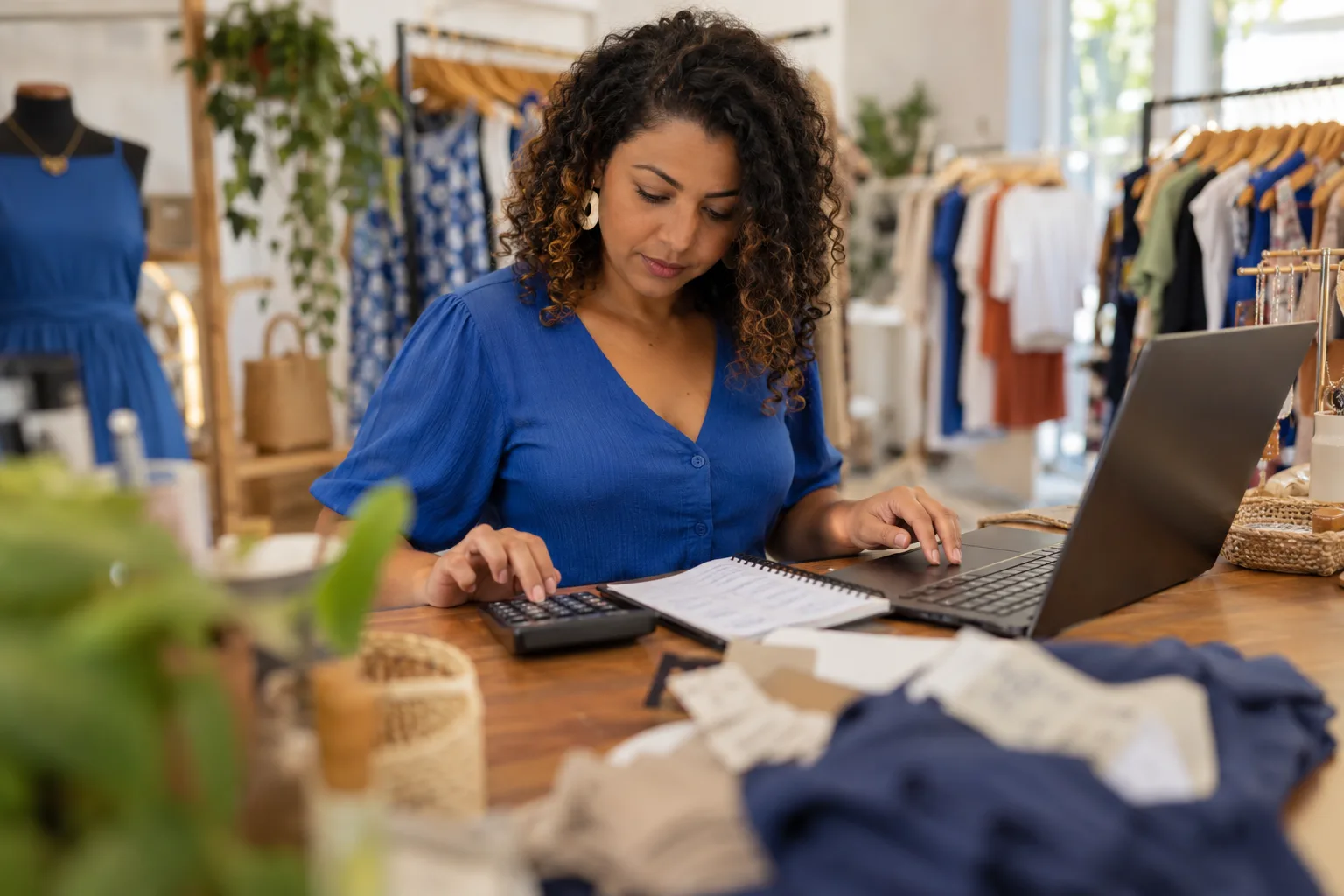 Dona de loja de roupas calcula preços com calculadora e notebook no balcão