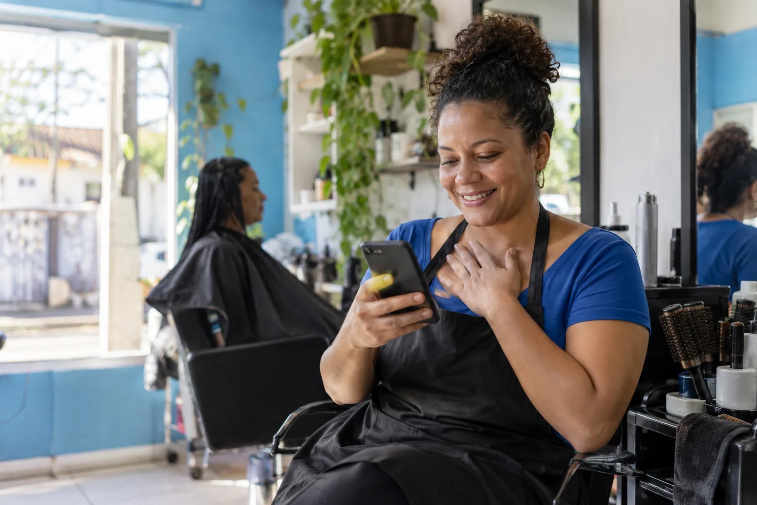 Cabeleireira microempreendedora confere o celular aliviada no próprio salão