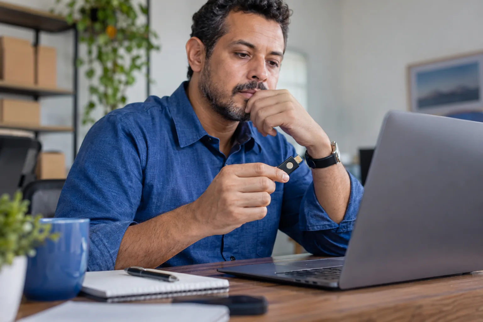 Empresário segura token de certificado digital ao lado do notebook no escritório