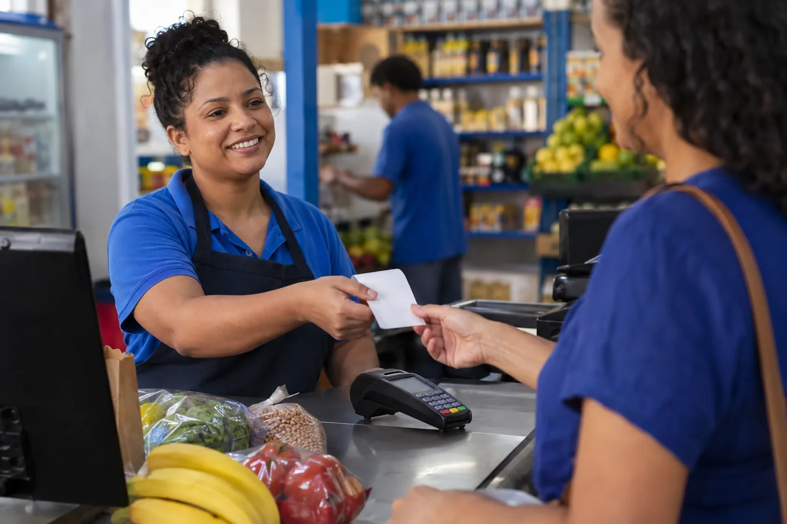Operadora de caixa de um mercado de bairro entrega o comprovante da compra para a cliente no balcão
