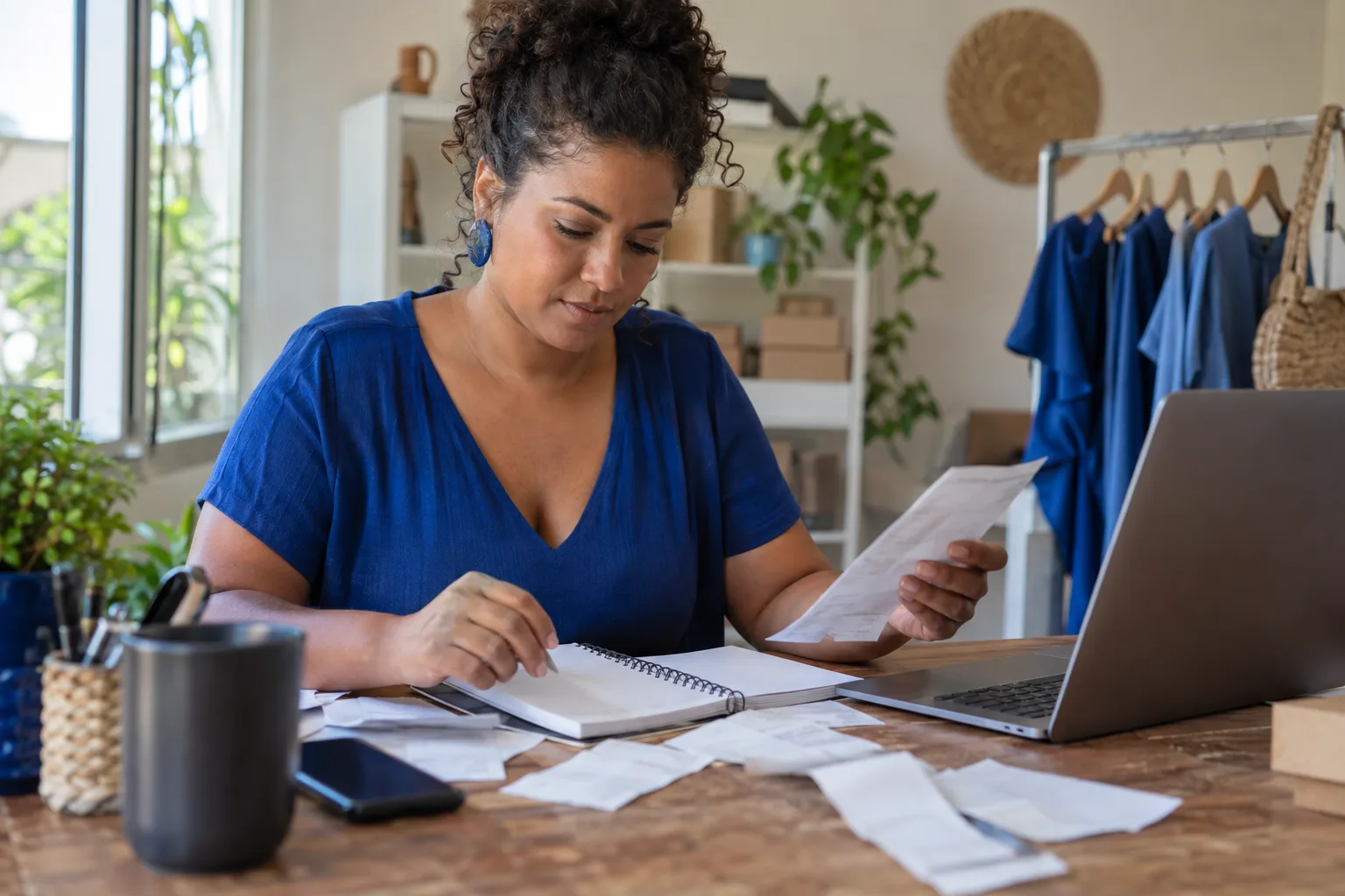 Microempreendedora confere o caderno de vendas e as notas do ano ao lado do notebook para fazer a declaração anual do MEI